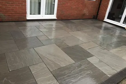 Grey sandstone patio slabs laid against a brick house with patio doors