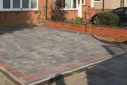 Grey block-paved front drive with a red brick border and a drainage channel