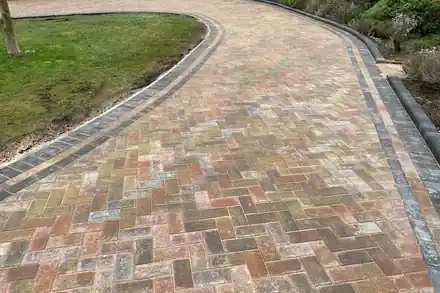 Curving block-paved drive in warm mixed tones with a dark border, beside a lawn